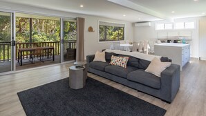 Ein modernes Wohnzimmer mit einem grauen Sofa, einem Couchtisch und einem schwarzen Teppich. Eine Glastür öffnet sich zu einem Balkon mit einem Holztisch und Stühlen.