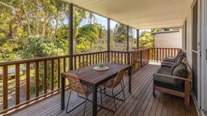 Eine Holzterrasse mit Tisch, Stühlen und einer Sitzecke, mit Blick auf Bäume und Grünflächen.