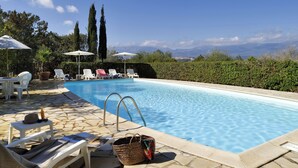 Une piscine entourée de verdure, avec des chaises longues et des parasols, et offrant une vue sur les montagnes.