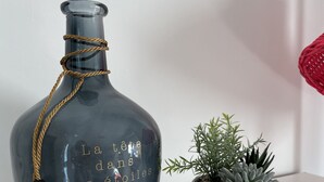 A dark blue bottle with gold text and a rope tied around its neck, placed next to a small potted succulent plant on a white surface. - Beach House (Lège-Cap-Ferret)