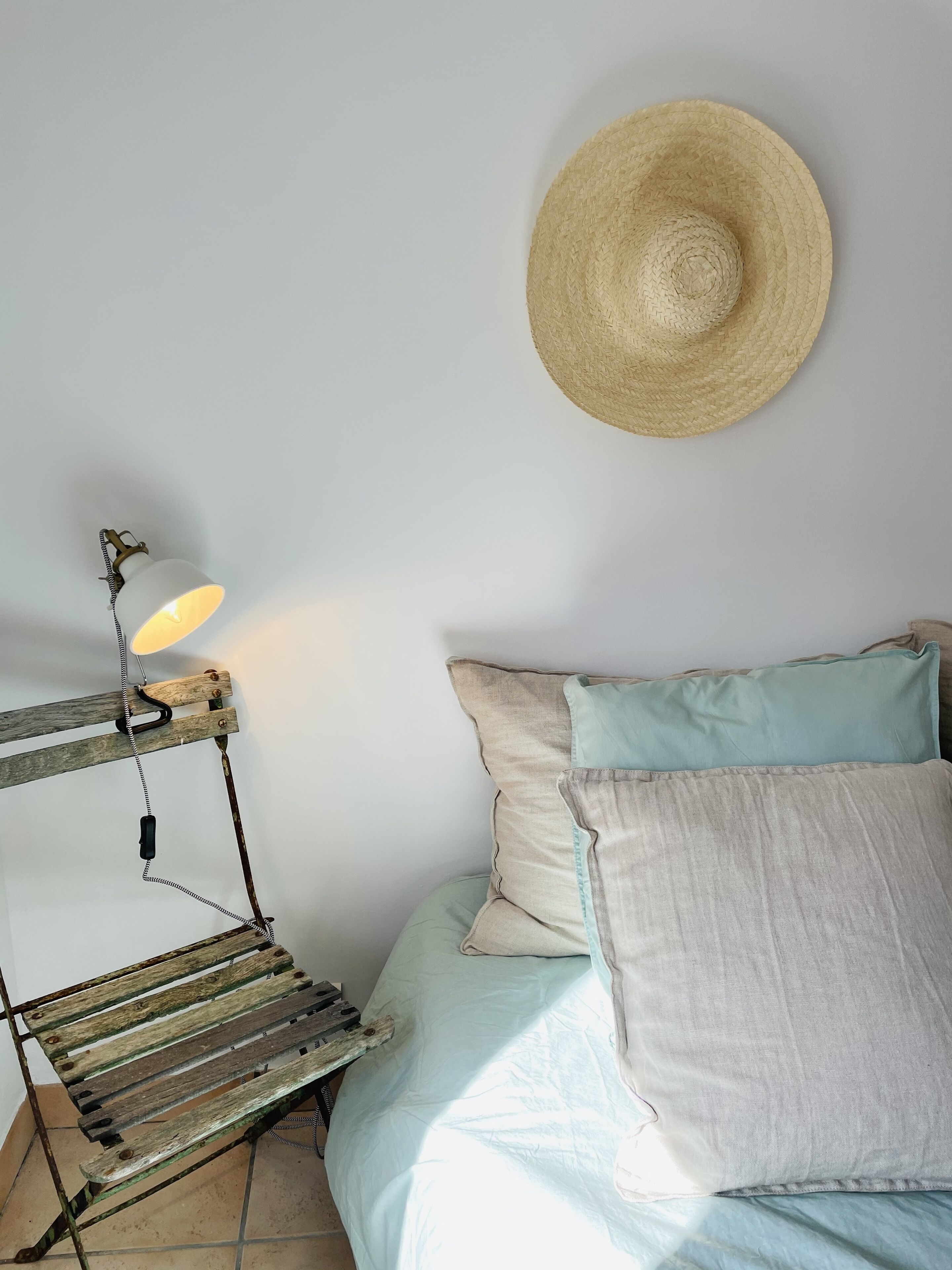 Une chambre à coucher avec un lit, des oreillers, un chapeau suspendu et une lampe ancienne.