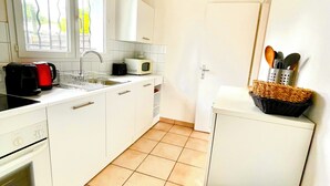 A compact kitchen with white cabinets, a microwave, a kettle, and a trash bin. - Beach House (Lège-Cap-Ferret)