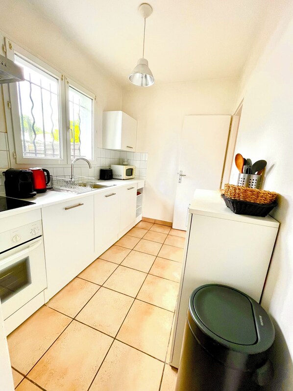 A compact kitchen with white cabinets, a microwave, a kettle, and a trash bin. - Beach House (Lège-Cap-Ferret)
