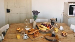 A dining table with a variety of food items, a vase with flowers, and a bowl of fruit. There are two metal pans hanging on the wall above the table. - Dolce Vivere by Konnect, Gaios Paxos (Paxos)