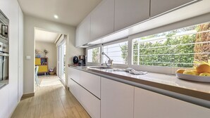 A modern kitchen with a long countertop, a coffee maker, and a window with a view of greenery. - Modern villa with private pool and garden (Mar de Cristal)