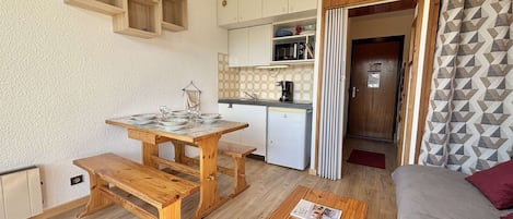 A compact living space with a wooden dining table, a bench, a small kitchenette, and a sofa.