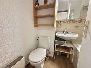 Ein kleines Badezimmer mit Toilette, Waschbecken und Spiegel. Über dem Waschbecken befindet sich ein Ablagefach und darunter ein Schrank.