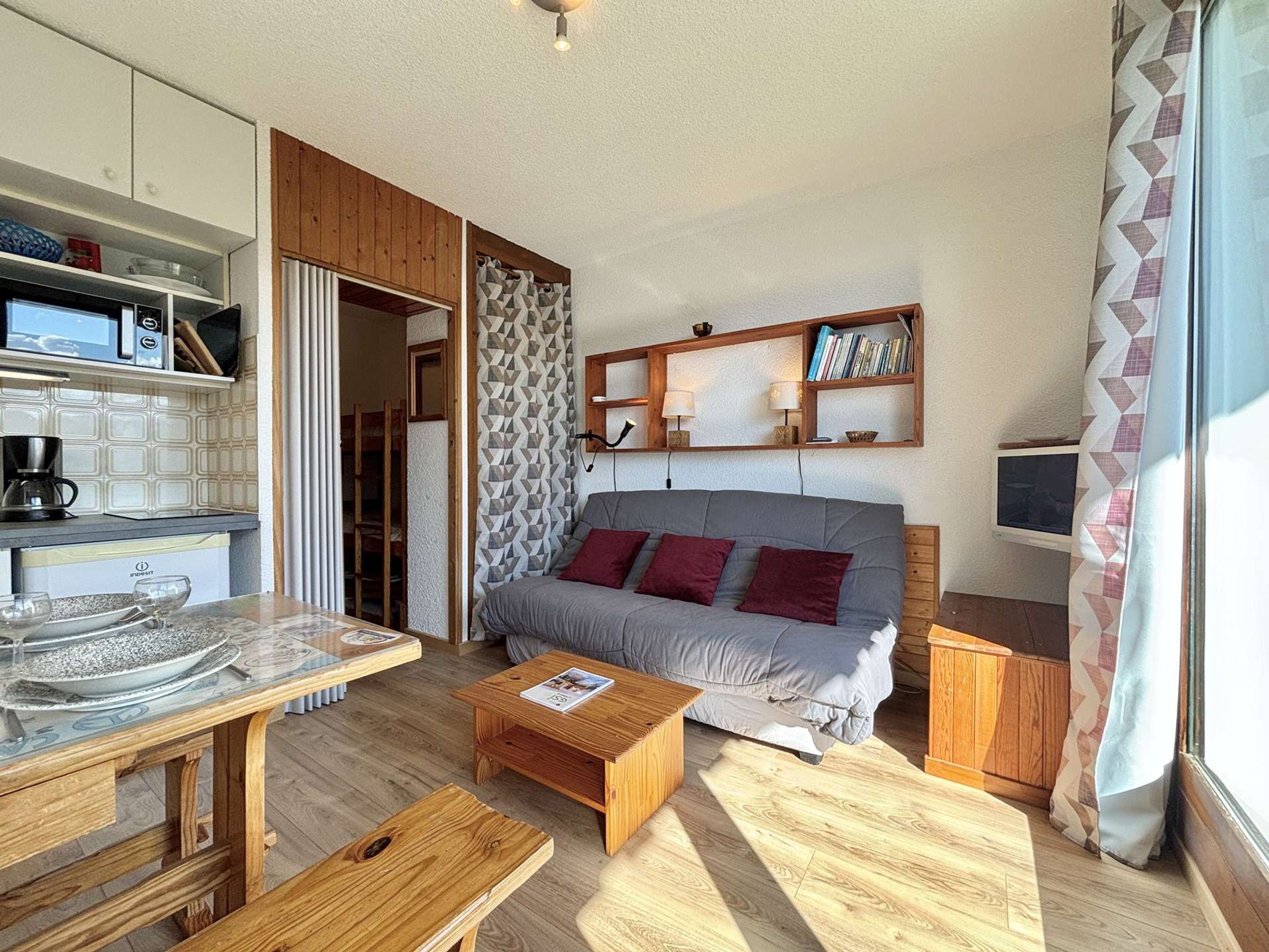 Un espacio habitable compacto con kitchenette, un sofá con cojines, una mesita de centro y un televisor.