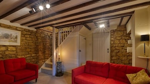 Un salon chaleureux avec un mur en pierre, un escalier et un canapé rouge.