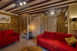 Ein Zimmer mit Steinwand, Holzbalken, einer Treppe und roten Sofas.