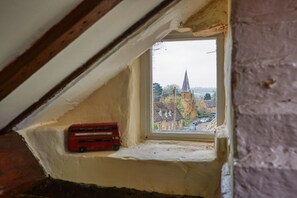 A small attic window with a view of a church and a red bus parked outside. - Fab 2-bed Cotswolds Cottage With Private Courtyard (Southam)