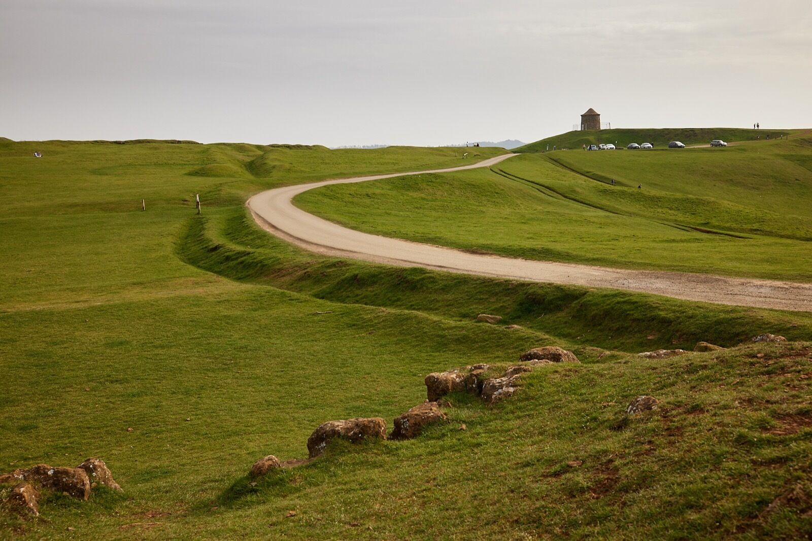 A winding road through a green landscape with a small building on a hill.