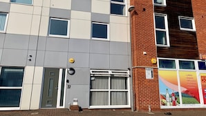 A multi-story building with a mix of brick and panel exteriors, featuring a variety of windows and a visible entrance with a door and gate. - Toothbrush Apartments - 2 Bed 1 Bath Apt (Ipswich)
