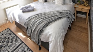 Une chambre avec un plafond en pente, un lit avec une literie à motifs, une table de chevet avec une lampe, et une vue par la fenêtre.