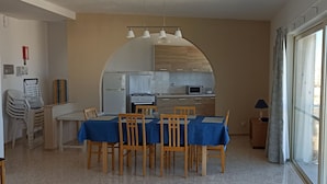 Une cuisine compacte dotée d’appareils électroménagers modernes, un coin repas avec une nappe bleue et une grande fenêtre agrémentée de rideaux.