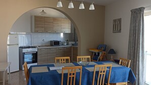Une cuisine compacte équipée d’un four à micro-ondes, d’une cuisinière et de placards, une table à manger avec des chaises, et une vue par la fenêtre.