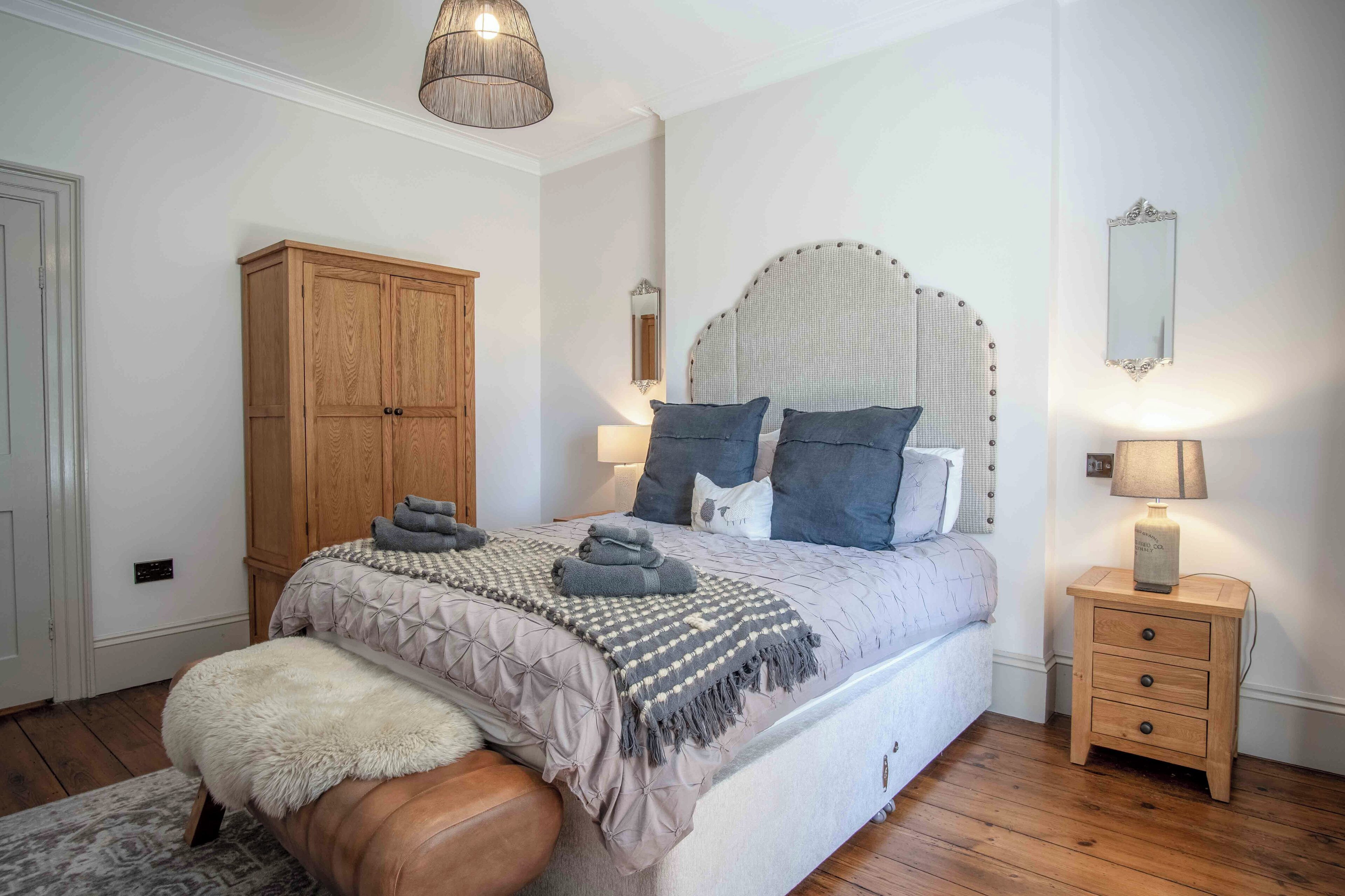 A bedroom with a bed, a wooden wardrobe, a nightstand, and a mirror.