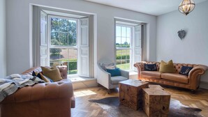A spacious living room with a large window, a leather sofa, a wooden coffee table, and a grey armchair. - Cilrhiw Country House - Narberth (Narberth)