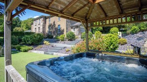A hot tub under a wooden pergola with a stone building in the background. - Cilrhiw Country House - Narberth (Narberth)