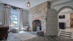 A cozy living room with a stone fireplace, a plush sofa, and a large window with curtains. - Cilrhiw Country House - Narberth (Narberth)