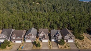 A residential area with multiple houses, each with a garage, set against a backdrop of dense forest and distant mountains.
