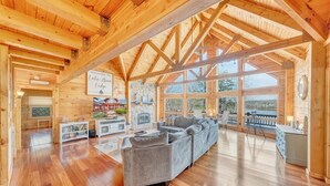 Een ruim houten blokhutinterieur met een grote bank, een stenen open haard en een bord dat gasten verwelkomt bij Lake Bear Lodge.