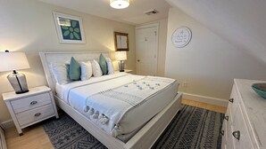 Ein Schlafzimmer mit einem Bett, Nachttischen, einer Kommode, einem gemusterten Teppich und einer Wand mit einem gerahmten Bild und einem Schild.