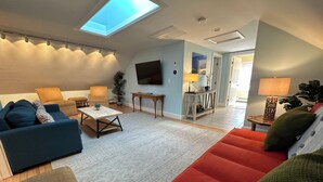 Ein modernes Wohnzimmer mit Sofa, Sessel, Couchtisch und einem an der Wand montierten Fernseher.