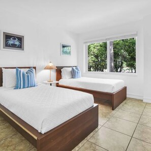 Een hotelkamer met twee bedden, een nachtkastje, een lamp en een raam met uitzicht op bomen.