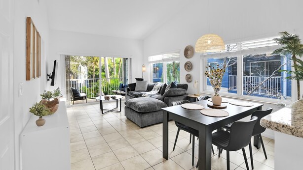 Een ruime woonkamer met een grijze modulaire bank, een eettafel met stoelen, en een balkon met uitzicht op groen.