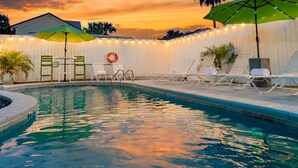 Piscina com espreguiçadeiras e guarda-sóis, cercada por um muro branco e luzes de fada.