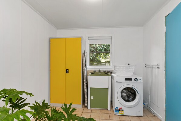 A laundry room with a yellow door, a green utility room, a window with a view of greenery, and a white washing machine.