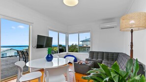 Enjoy ocean views from the large window in this stylish living room, featuring a round table, sofa, and flat-screen TV.