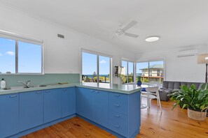 A modern kitchen with blue cabinets, a large window, and a view of the ocean.