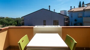 A balcony with a table and chairs, a white wall, and a building in the background. - S232 - Sirolo, delightful two-room apartment with terrace (Sirolo)