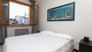 A bedroom with a bed, a window with curtains, a radiator, a painting of an underwater scene, and a dresser. - S232 - Sirolo, delightful two-room apartment with terrace (Sirolo)
