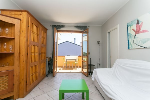 A room with a green table, a white sofa, a wooden cabinet, and a sliding glass door leading to an outdoor area with a table and chairs.