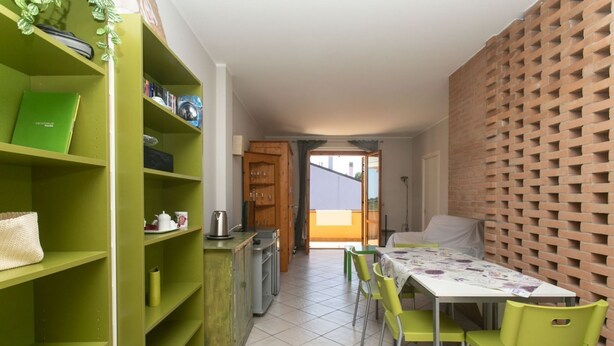 A room with a dining table, chairs, a green bookshelf, a kitchen area, and a brick wall. - S232 - Sirolo, delightful two-room apartment with terrace (Sirolo)