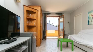 A room with a television, a wooden cabinet with wine glasses, a green table, and a white sofa. - S232 - Sirolo, delightful two-room apartment with terrace (Sirolo)