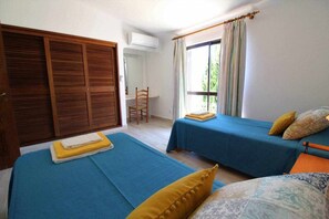 Une chambre avec deux lits, une chaise, une fenêtre avec des rideaux et une armoire.