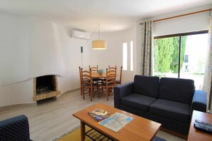 A living room with a fireplace, a sofa, a dining table with chairs, and a large window with curtains.
