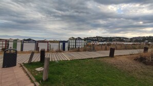 A beachside walkway leading to beach huts with a view of a town and water in the background.