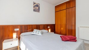 A bedroom with a bed, wooden wardrobe, nightstands, and a wall-mounted light fixture.