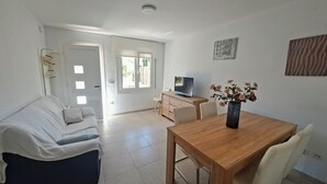 A living room with a sofa, a wooden dining table, a TV, and a vase with flowers.