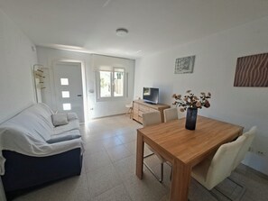 A living room with a sofa, a wooden dining table, a TV, and a vase with flowers.