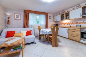 Un espace de vie compact comprenant un canapé, une table à manger, des chaises, un petit coin cuisine avec des placards et une cuisinière, ainsi qu’une fenêtre avec des rideaux.