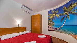 Ett hotellrum med en säng, en garderob, en luftkonditioneringsanläggning och en väggmålning som föreställer en strandscen.