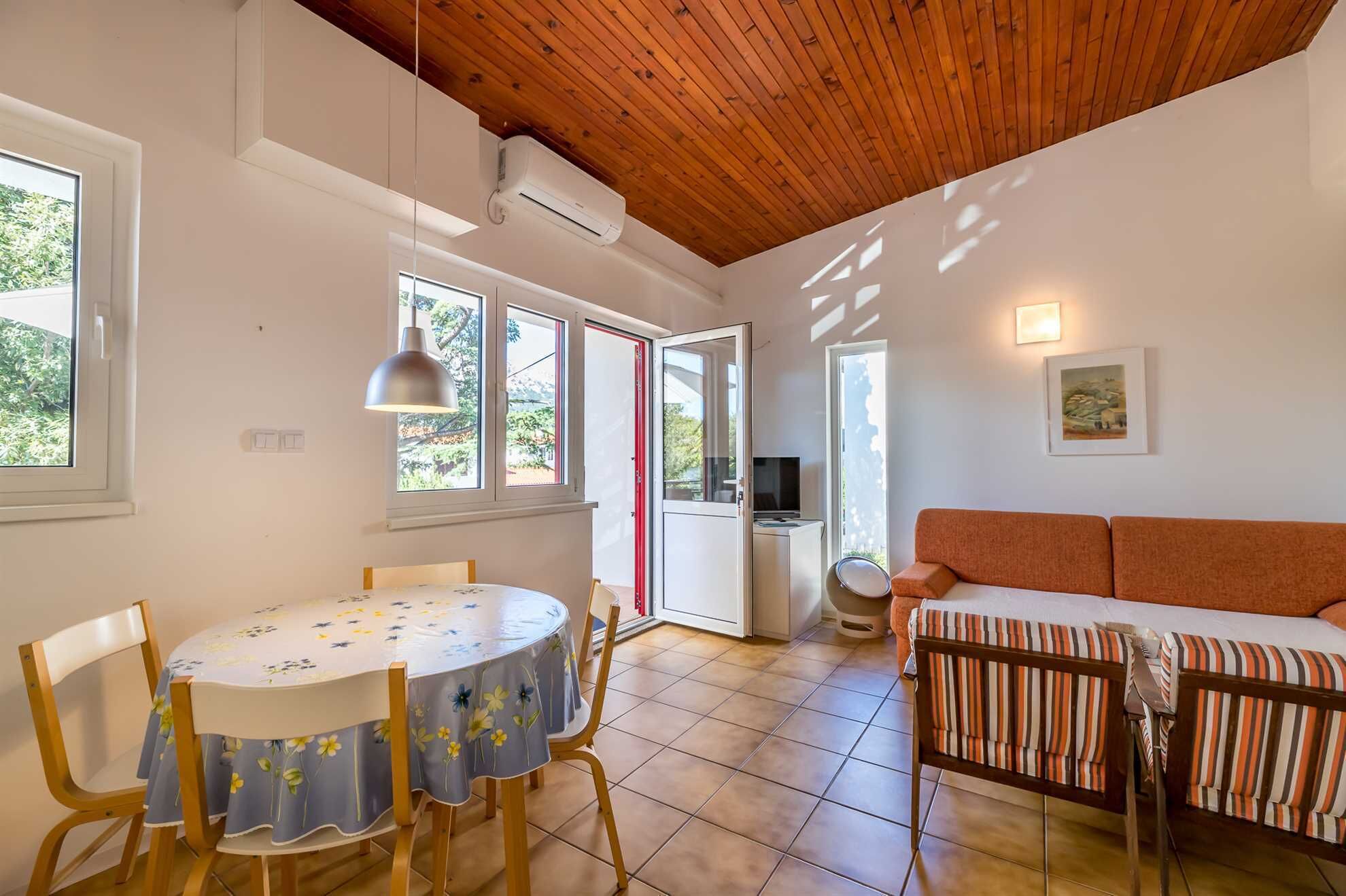 Une pièce avec un plafond en bois, une table à manger avec des chaises, un canapé et un téléviseur posé sur un meuble.