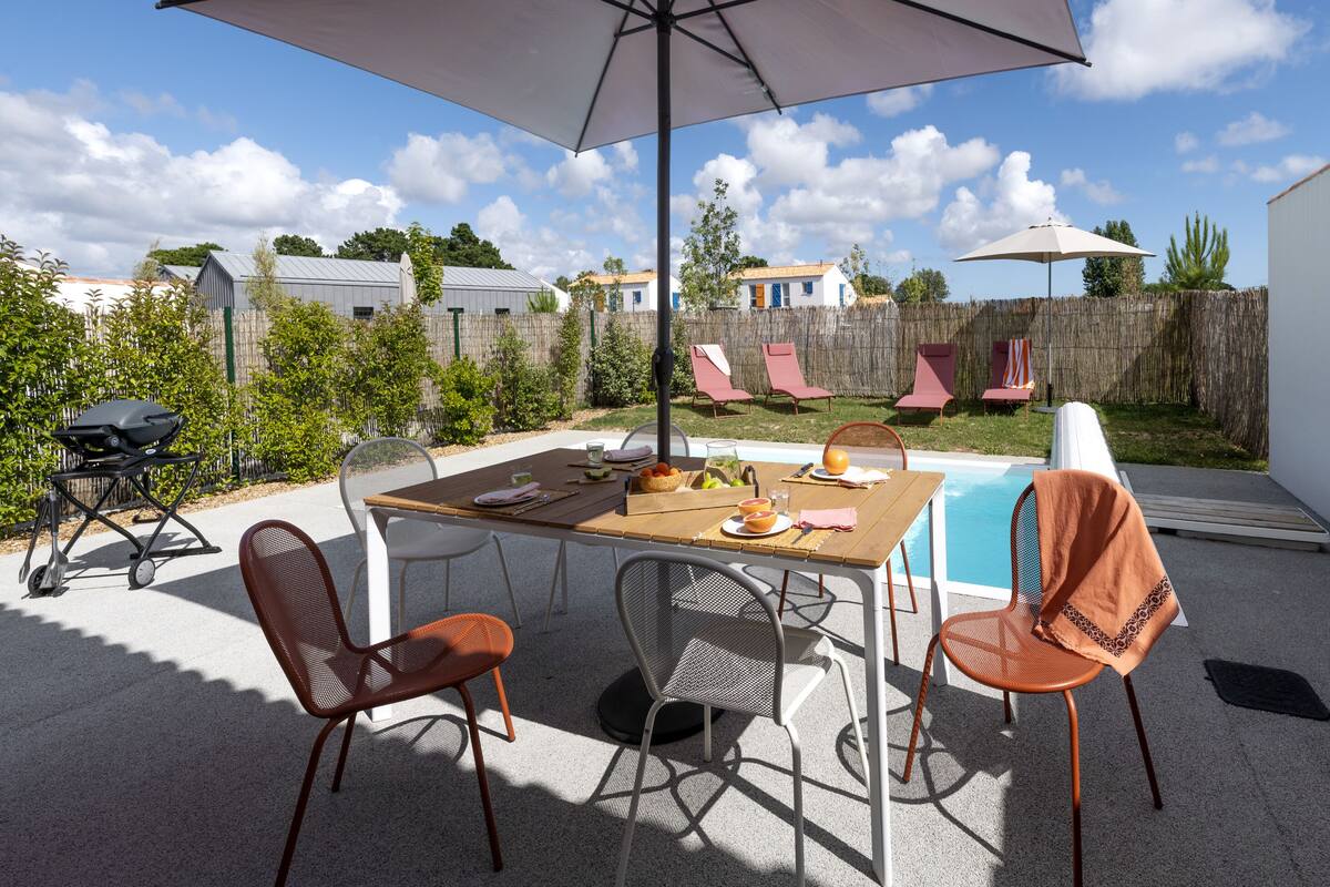 Un patio exterior con piscina, una mesa lista para comer y sillas.