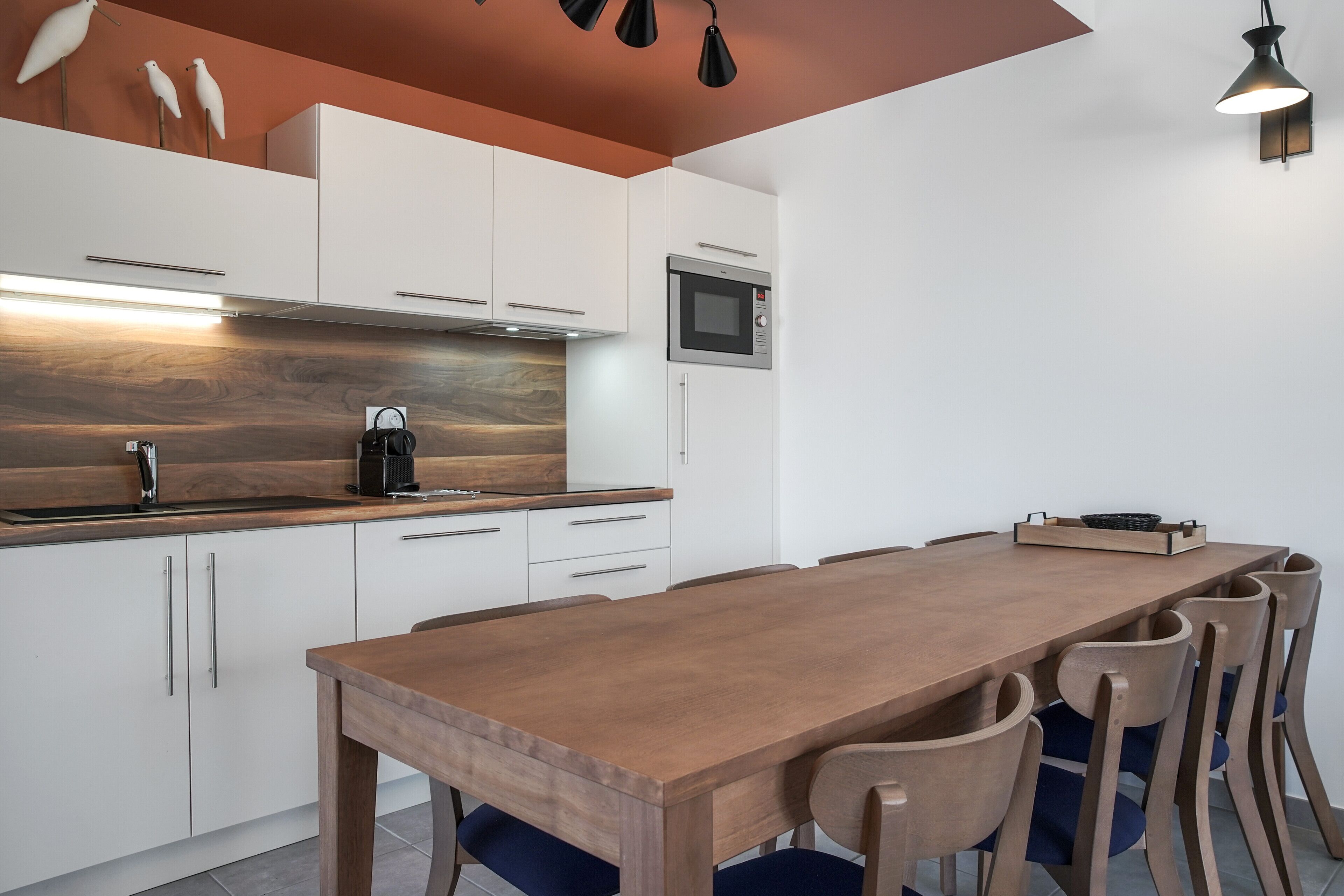Une cuisine moderne avec des armoires blanches, un comptoir en bois, un four à micro-ondes encastré et une table à manger en bois avec des chaises.